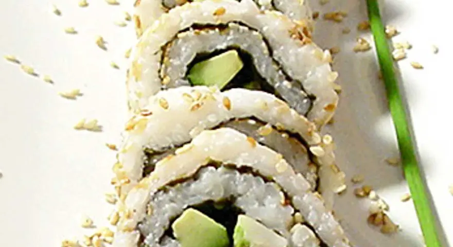 En närbild på en california roll med sesamfrön och en grön garnityr.