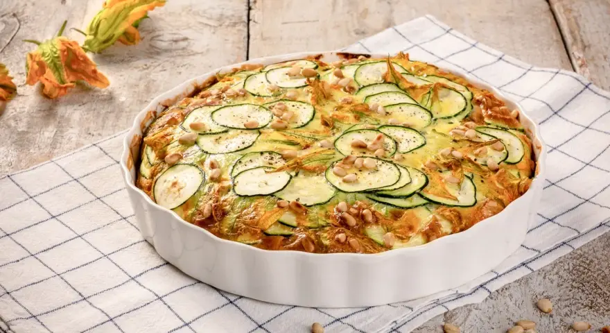 Frittata di zucchine al forno, guarnita con pinoli e fiori di zucca, pronta per essere gustata.