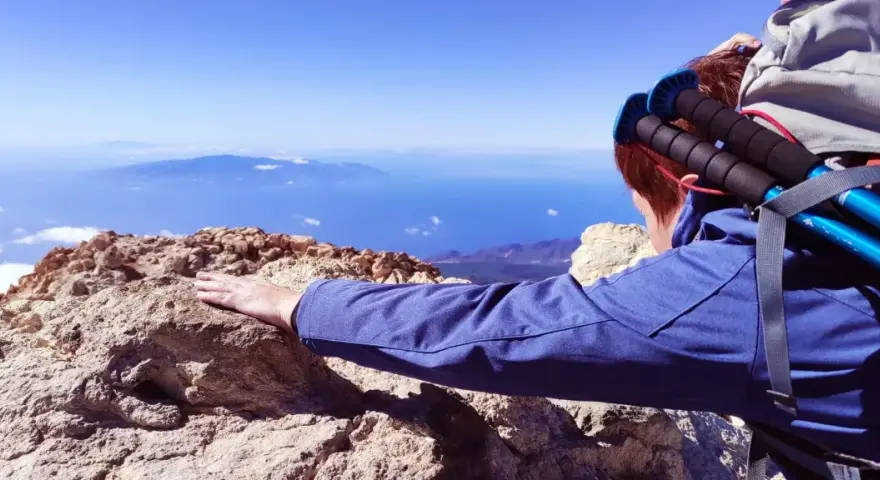Blick vom Gipfel nach der Teide Wanderung. Ein Wanderer lehnt sich auf Felsen, mit Blick auf das weite Meer und ferne Inseln.