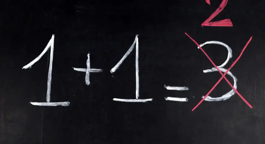 Na czarnej tablicy napisano kredą: 1+1=3. Dwójka jest podkreślona na czerwono, a trójka przekreślona. Jak na egzaminie dojrzałości, gdzie liczy się poprawna odpowiedź.