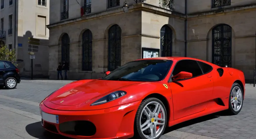 Czerwone Ferrari F430 zaparkowane na brukowanej ulicy przed kamienną kamienicą.