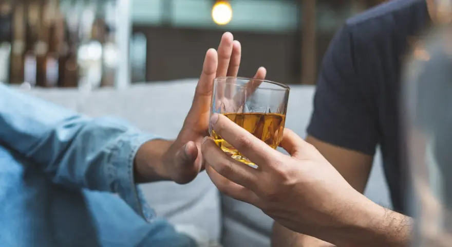 Dłoń odrzuca szklankę z alkoholem. Przykład asertywnego odmawiania picia alkoholu.