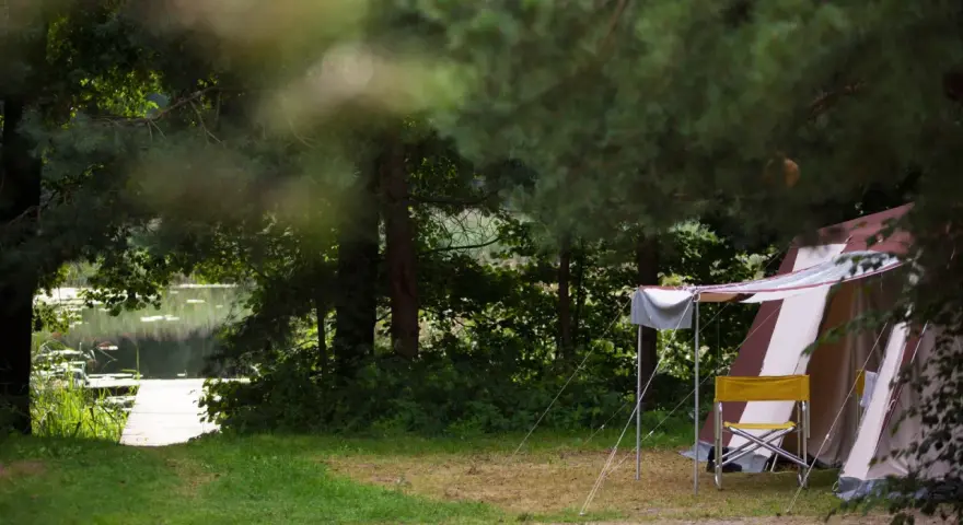 Namiot i krzesło na tle jeziora i lasu. Idealne pola namiotowe Mazury dla miłośników natury.