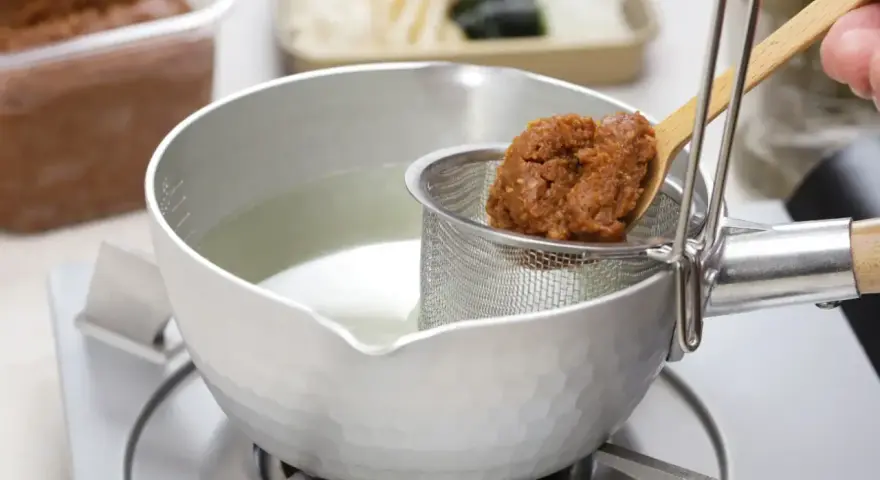 Łyżka z pastą miso trafia do bulionu. Tak przygotowuje się bazę do zupy, pytasz miso co to? To fermentowana pasta sojowa.