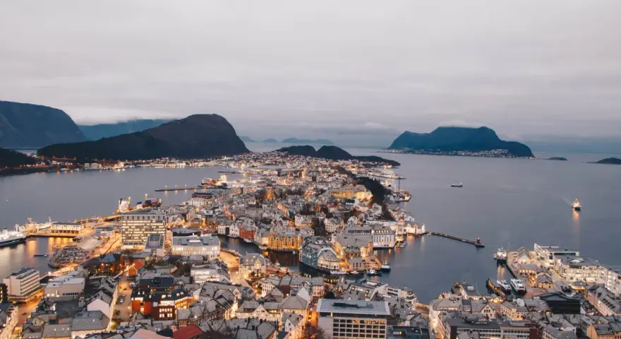 Vacker stad vid vattnet i Norge, med upplysta hus och berg i bakgrunden. En dröm att bila i Norge.