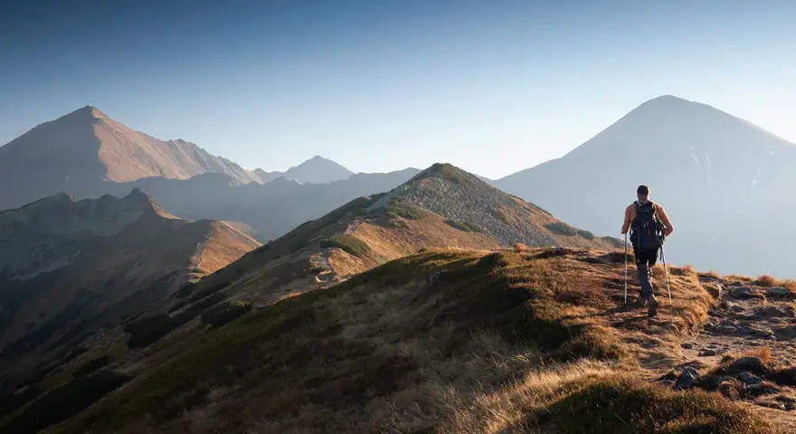 Wędrowiec na grani Tatr, odkrywa malownicze tatry szlaki dla średnio zaawansowanych. Słońce oświetla zbocza.