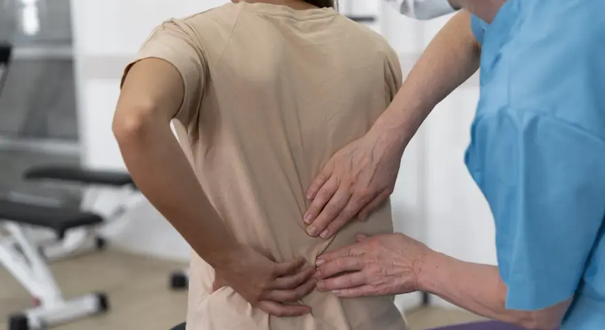 Fizjoterapeuta bada plecy pacjentki, która odczuwa ból po upadku na plecy. Konsekwencje urazu są widoczne.