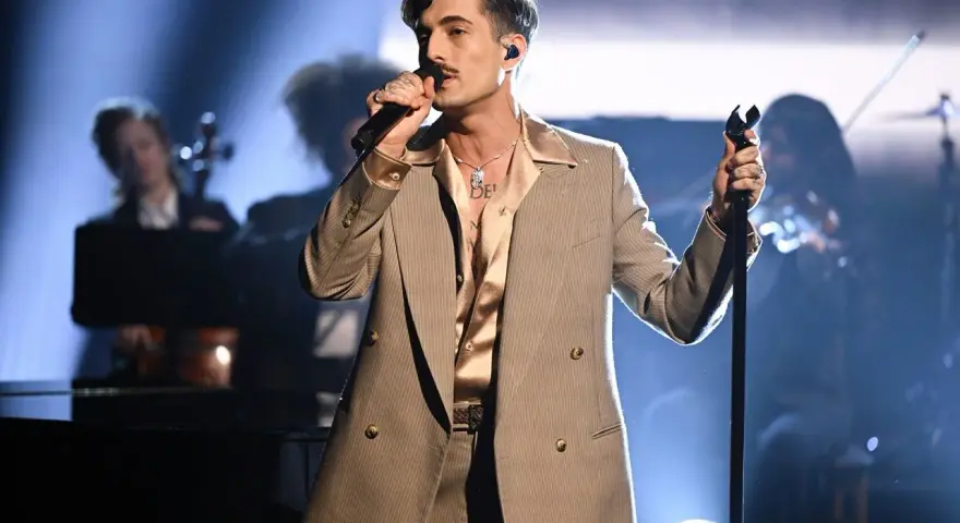 Un cantante con un completo gessato e camicia satinata, microfono in mano, incarna il **dandy significato** con stile sul palco.