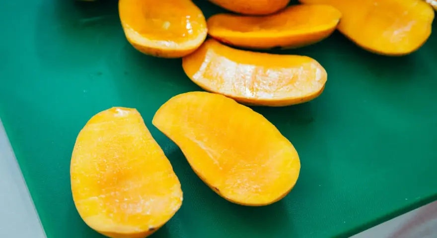 Pokrojone w łódeczki, soczyste mango w intensywnym kolorze, jakby w ciąży z owocową obfitością, leżą na zielonej desce.