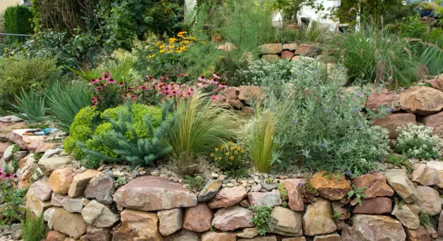 Ein wunderschöner Steingarten, der zeigt, wie man mit wenig Geld einen tollen Garten gestalten kann. Bunte Blumen und Gräser wachsen zwischen Natursteinen.