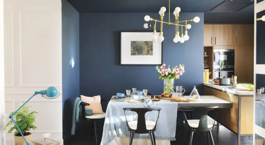 El azul oscuro combina con tonos pastel, madera y dorado. Un comedor elegante con mesa, sillas negras, lámpara dorada y flores.