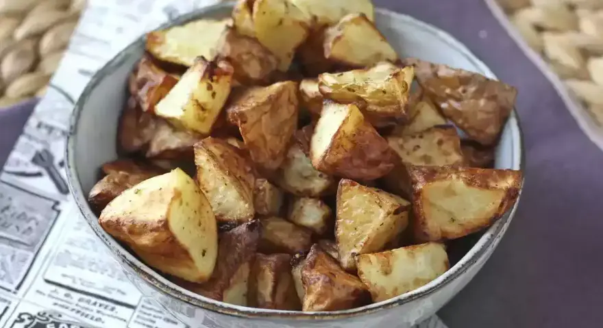 Patate dorate e croccanti in friggitrice ad aria, servite in una ciotola su carta di giornale.