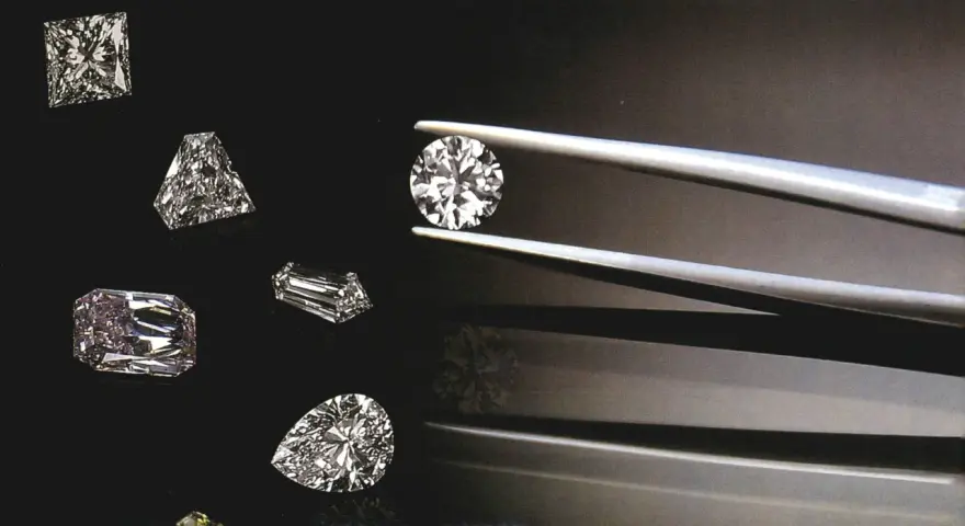 Diverse pietre preziose, tra cui diamanti, brillano su sfondo scuro. Una pinzetta tiene un diamante rotondo, mentre altri, di varie forme, sono disposti intorno.