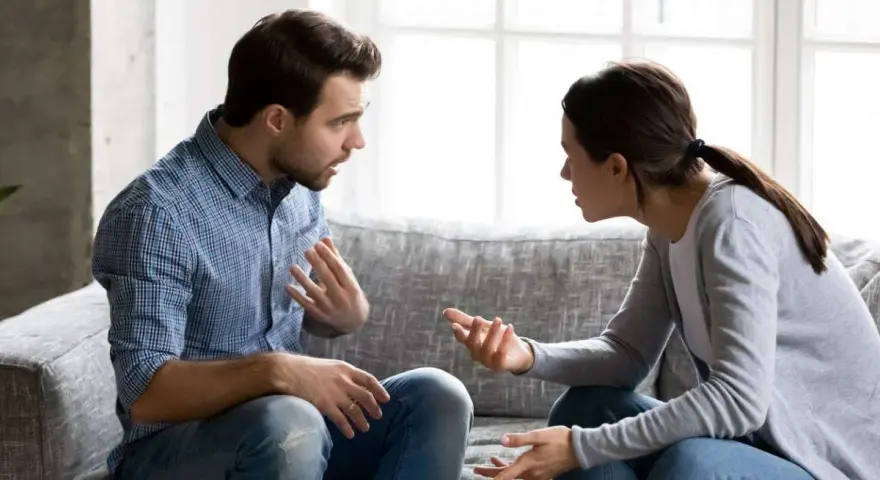 Un couple discute sur un canapé, les mains tendues, peut-être lors d'une séance de thérapie de couple pour améliorer leur communication.