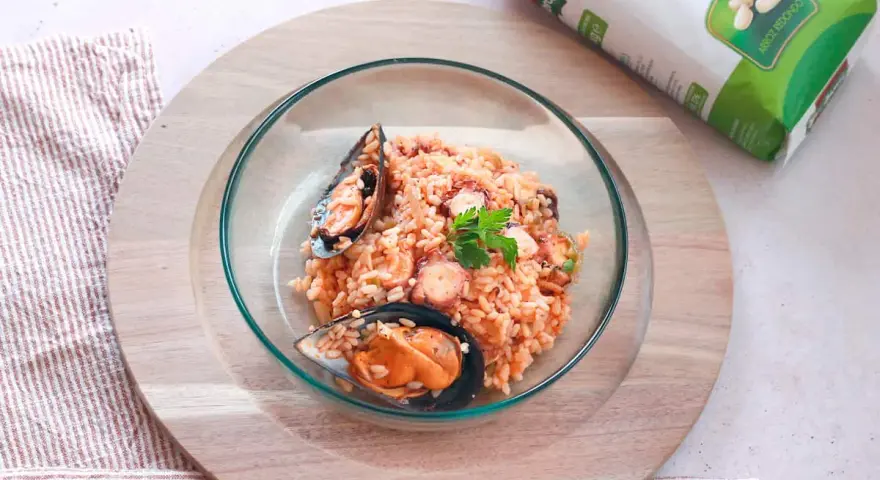 Delicioso arroz con pulpo y mejillones, servido en un cuenco de cristal sobre una tabla de madera.