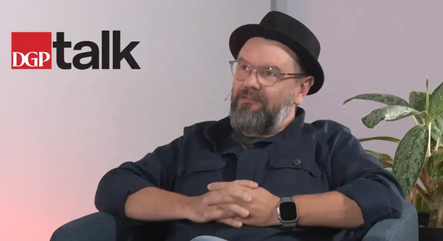 Mężczyzna w okularach i kapeluszu siedzi, rozmawiając. Obok logo DGP talk.