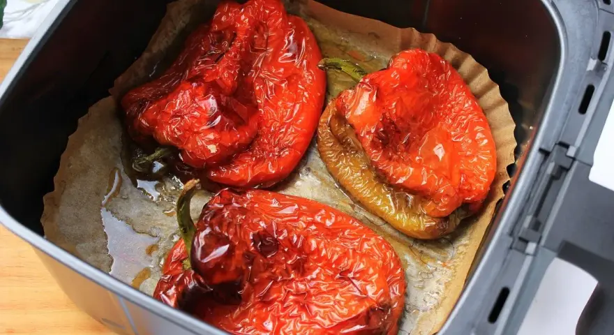 Tres pimientos rojos asados en freidora de aire, con la piel arrugada y jugosos, listos para disfrutar.