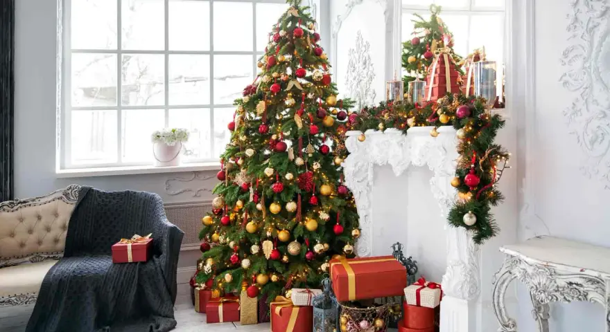 Un albero rosso, oro e bianco, addobbato con luci e palline, fa da protagonista in un salotto natalizio.