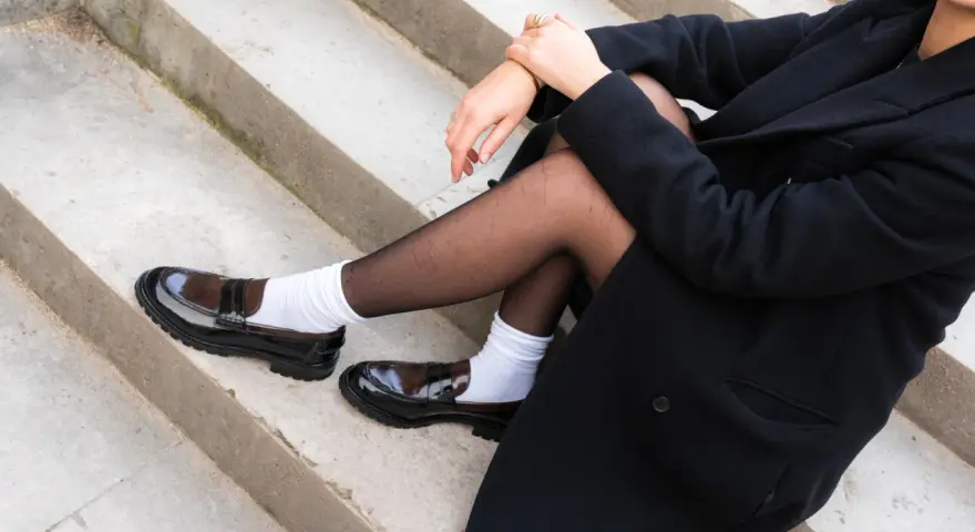 Białe skarpetki do mokasynów i czarny płaszcz na betonowych schodach. Stylowy look.