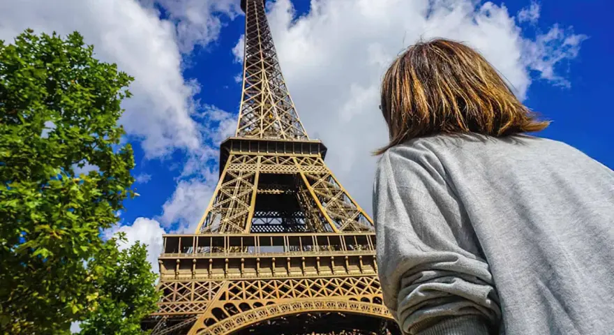 Persona admira la imponente Torre Eiffel bajo un cielo azul con nubes.