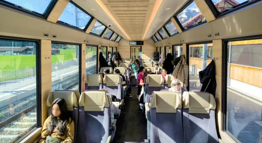 Passengers enjoy the scenic views from the panoramic windows of a train on the Golden Pass Line, with mountains visible outside.