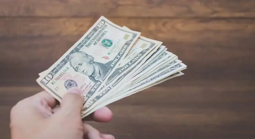Dłoń trzyma plik banknotów dziesięciodolarowych. To może być zapłata za trzynastkę lub po prostu nagroda.