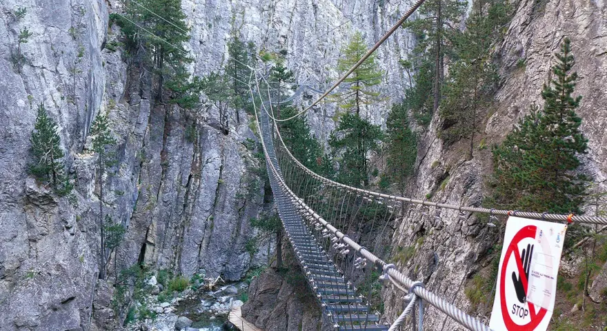 Un emozionante ponte tibetano in Piemonte attraversa una gola rocciosa, con un torrente sottostante e pini aggrappati alle pareti.