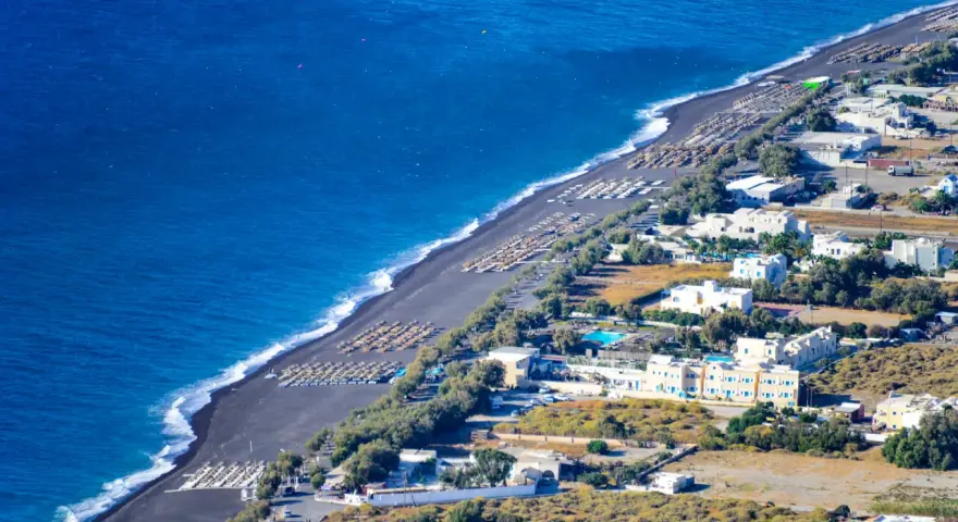 Santorini plaże z czarnym piaskiem, rzędy leżaków i białe budynki hotelowe nad turkusowym morzem.