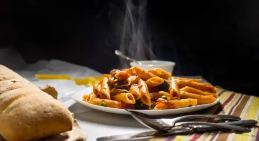Piatto fumante di penne alla vodka, con pane croccante e posate. Un classico confortante.