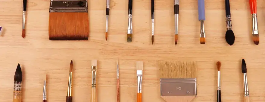 Collection de différents types de pinceaux peinture, ronds et plats, aux poils variés, disposés sur un fond en bois.
