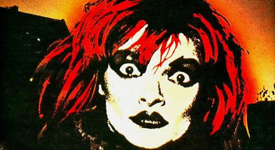 Visage intense d'une femme aux cheveux rouges et maquillage prononcé, évoquant l'esthétique d'un groupe allemand des années 90.