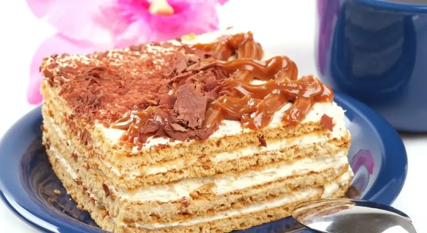 Szybkie ciasto z mlekiem skondensowanym, przełożone kremem i posypane czekoladą, wygląda pysznie obok niebieskiej filiżanki.