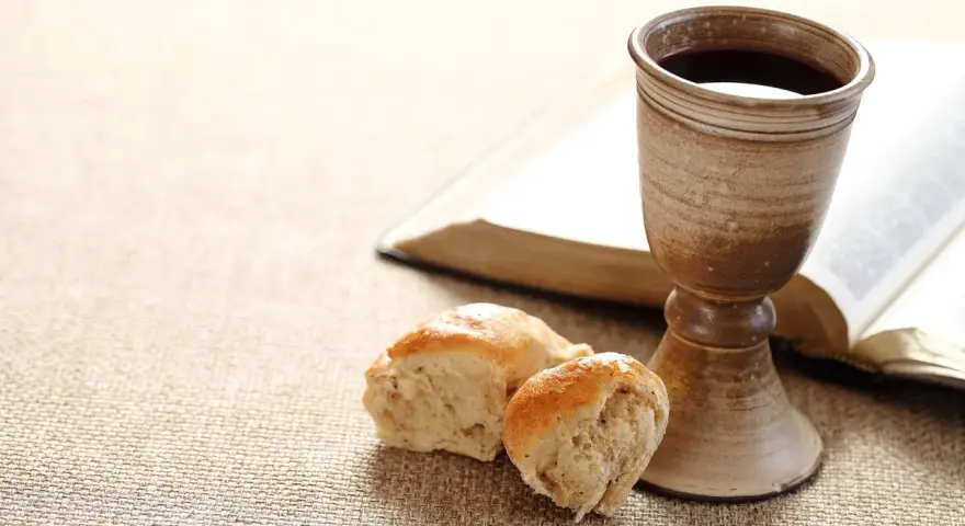 Kelch mit Rotwein, Brot und aufgeschlagenes Buch. Symbol für das christliche Abendmahl und dessen Bedeutung im Glauben.