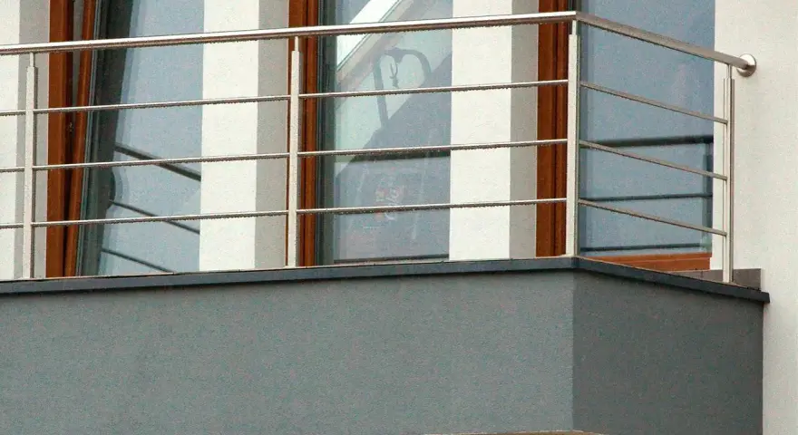 Nowoczesne mocowanie balustrady od czoła balkonu, wykonane ze stali nierdzewnej, z widocznymi czterema poziomymi prętami.