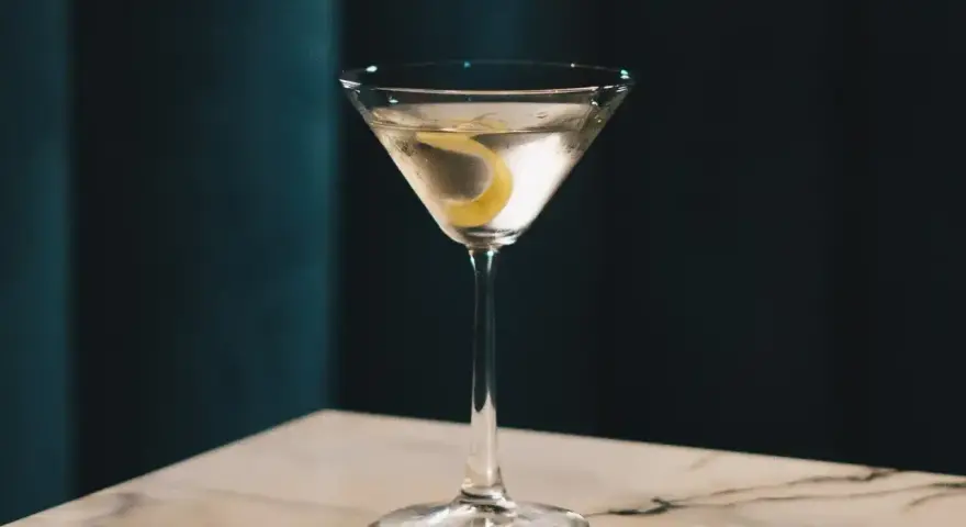 Elegancki gin z wermutem, ozdobiony skórką cytryny, czeka na stole z marmurowym blatem.