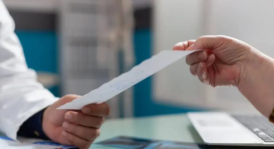 Lekarz w białym fartuchu podaje pacjentowi dokument.