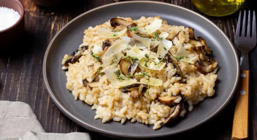 Kremowe risotto z pieczarkami, posypane parmezanem i ziołami, na ciemnym talerzu.