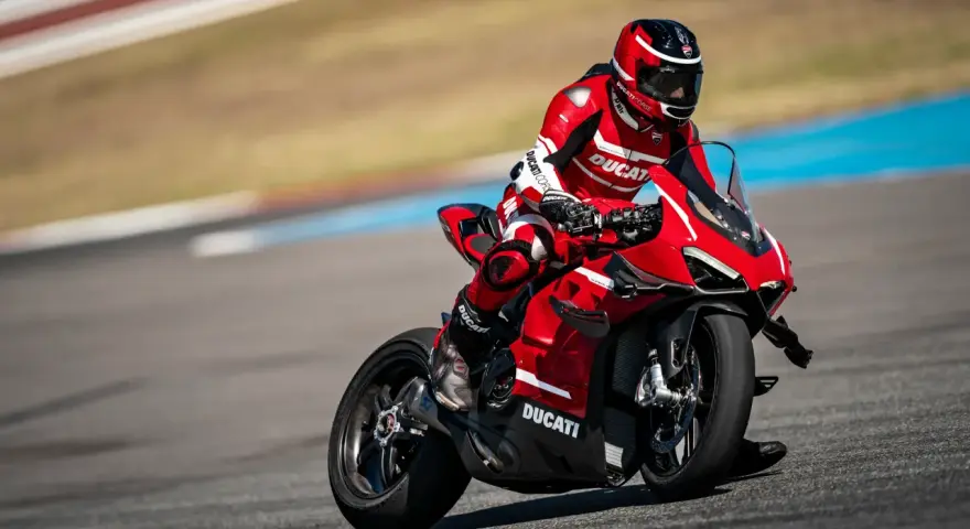 Motocyklista w czerwonym kombinezonie śmiga na torze wyścigowym na swoim czerwonym Ducati Panigale V4.