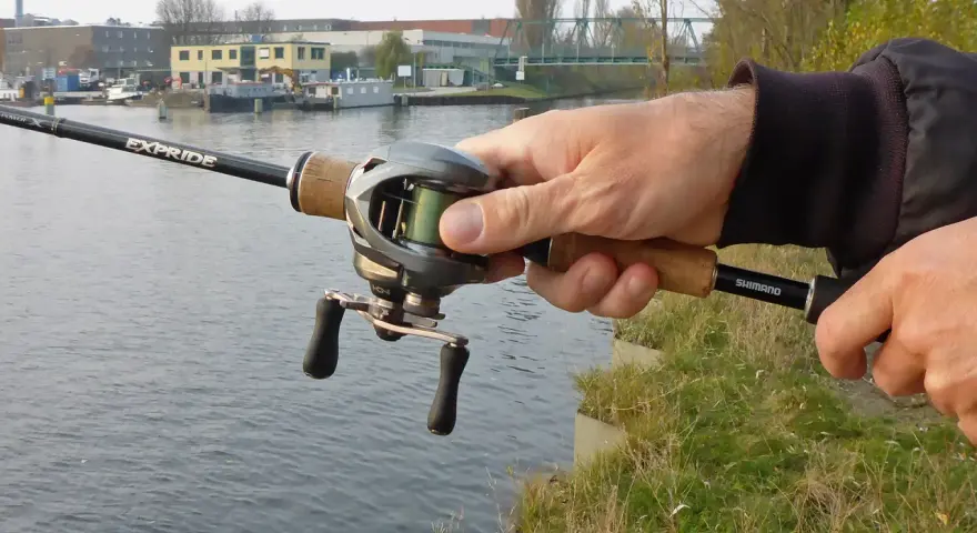 Hand hält Angelrute mit Baitcast-Rolle, die grüne baitcast schnur ist gut sichtbar.