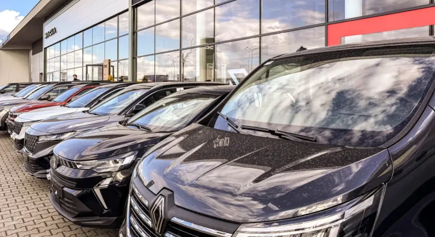 Rząd nowych samochodów na placu. W tle budynek salonu Dacia. Sprawdź autoplac opinie przed zakupem.