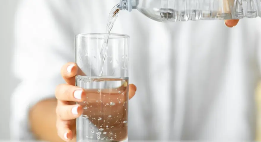 Eine Hand hält ein Glas, in das kohlensäurehaltiges Mineralwasser gegossen wird.