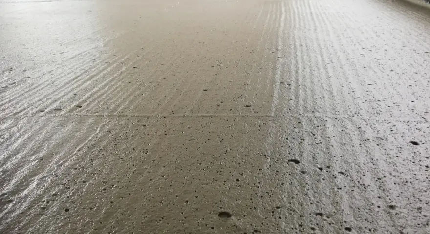 Świeżo wylany, wilgotny **pianobeton** na budowie, z widocznymi śladami po zacieraniu i drobnymi pęcherzykami powietrza.