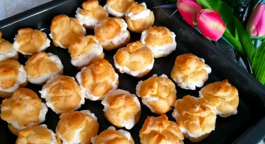 Pyszne ciasto na ptysie, wypełnione kremem, czeka na spróbowanie. Obok piękne tulipany.