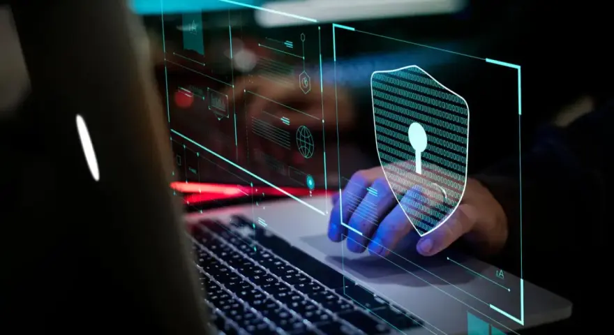 Mano sobre teclado de portátil, con un escudo digital de ceros y unos, simbolizando la seguridad informática.