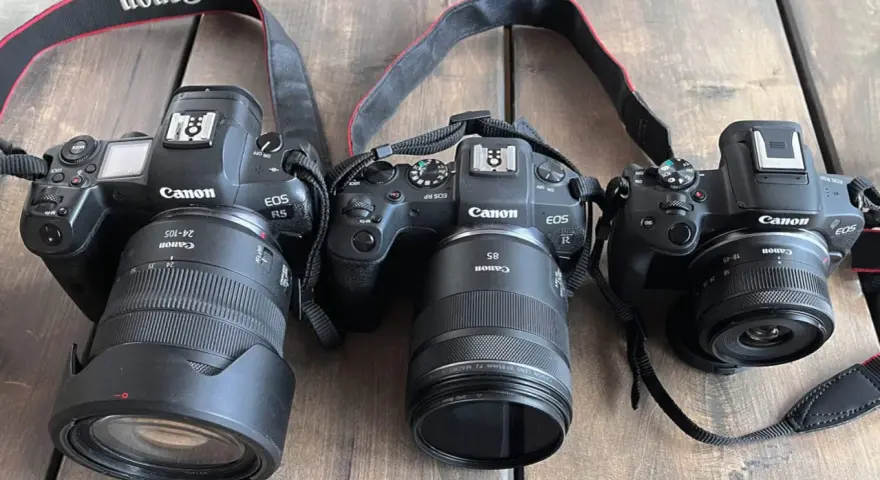 Trzy aparaty Canon EOS R, RP i R5 leżą obok siebie na drewnianym blacie. To **pełna klatka** sprzętu fotograficznego.