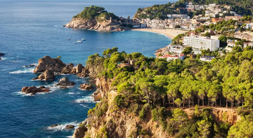 Scenic view of the Costa Brava coastline, a perfect stop on the way to Barcelona, with rugged cliffs, pine forests, and a charming town nestled by the sea.
