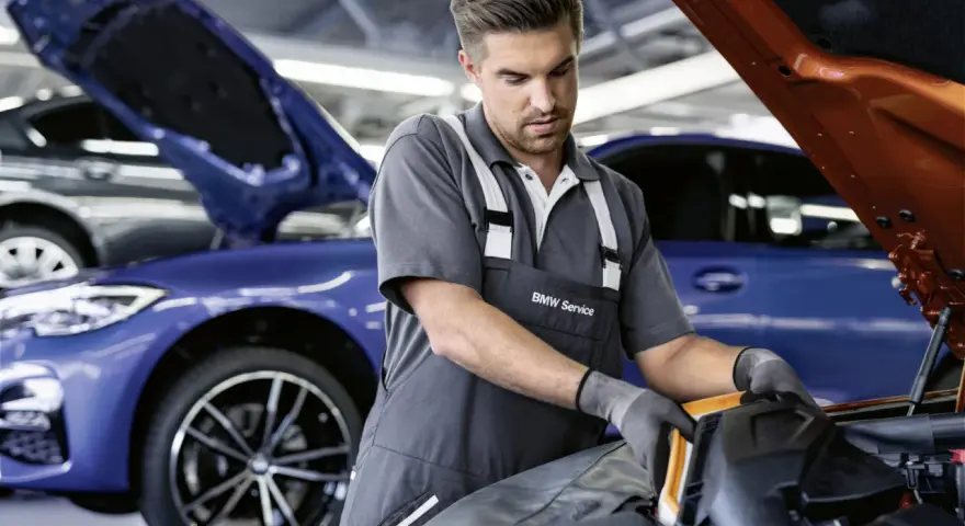 Mechaniker mit BMW Service Kleidung arbeitet an einem blauen BMW. Transparente Kosten für BMW Service.