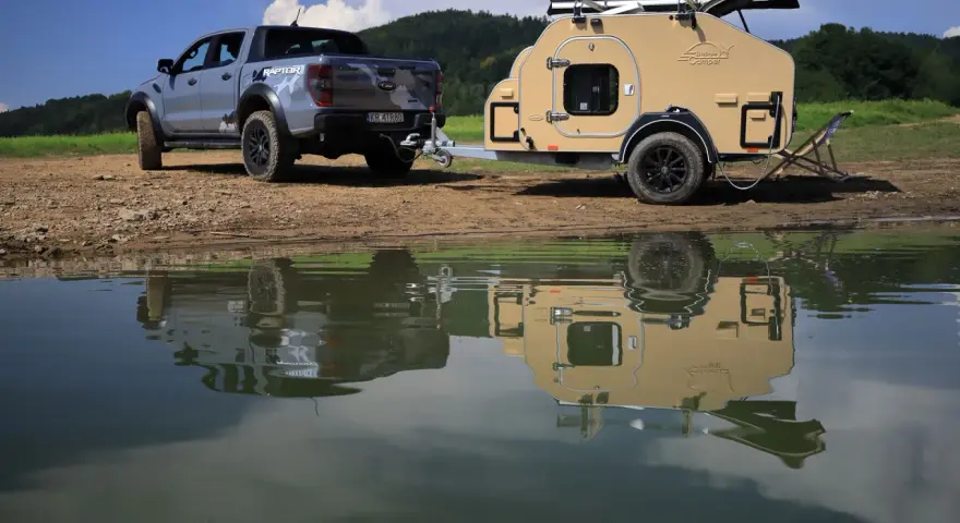 Srebrny Ford Raptor z przyczepą wyprawową Lifestyle Camper nad jeziorem.