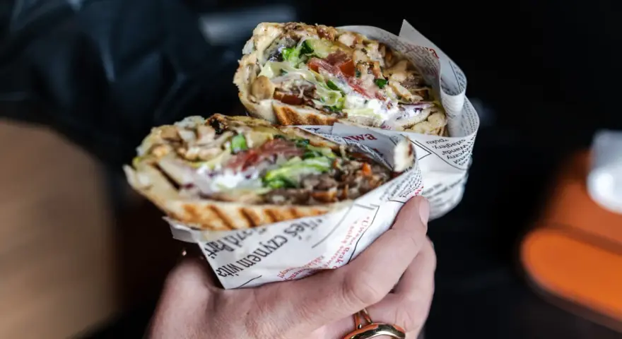 Pyszny kebab z Bukowiny Tatrzańskiej, pełen mięsa, warzyw i sosu, zawinięty w papier z gazetowym nadrukiem.
