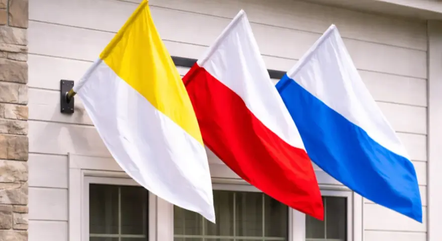 Trzy flagi: żółto-biała, czerwono-biała i niebiesko-biała, powiewają na wietrze. To może być flaga kościelna lub symbol parafii.